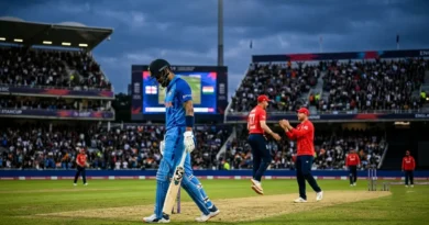 A disappointed Indian batsman walking off the cricket pitch while England players celebrate in the background during a T20 match in a crowded stadium.