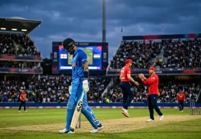 A disappointed Indian batsman walking off the cricket pitch while England players celebrate in the background during a T20 match in a crowded stadium.