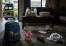 A dramatic symbolic scene inside a house in Kahna Lahore with children school bag, toys, grocery bag on table, and an Edhi ambulance outside the door.